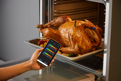 Person holding a smartphone with a cooking app over a roasted turkey in an oven.